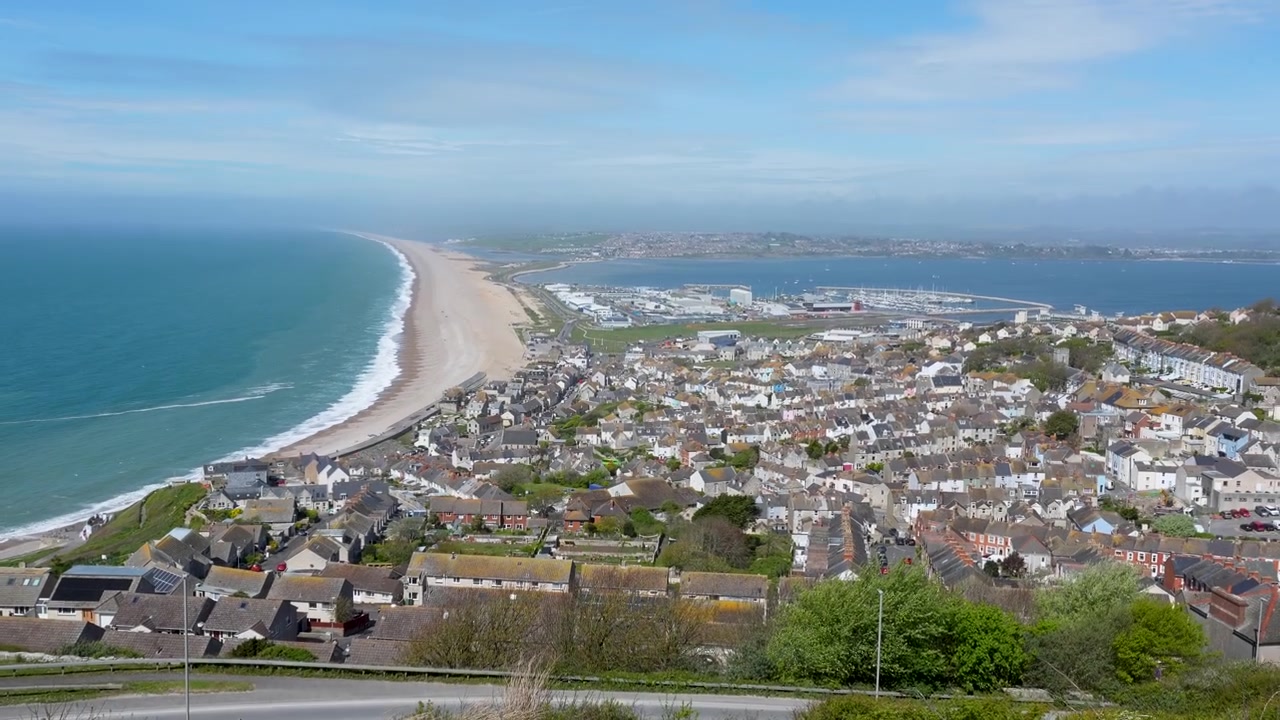 Un'inquadratura cinematografica dall'alto che mostra le fitte abitazioni residenziali e la costa di Weymouth e Portland, Dorset. Ideale per documentari di viaggio e marketing immobiliare.