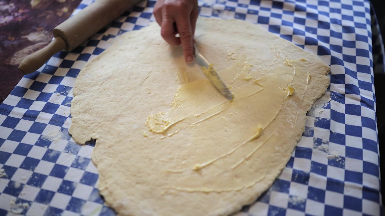 Butter is spread onto flattened dough when making cinnamon buns at home
