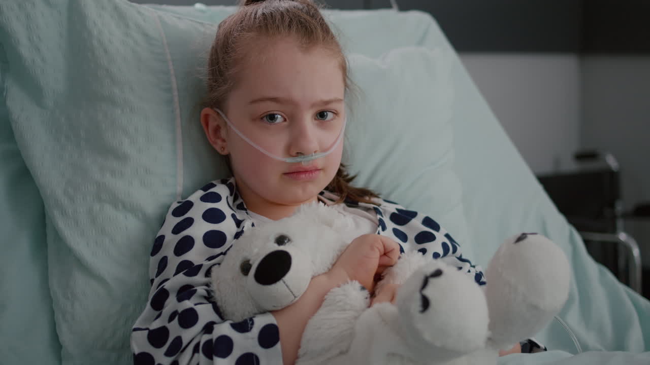 Portrait of little girl patient wearing oxygen nasal tube resting in bed recovery