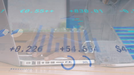 animación de datos financieros y gráficos que se mueven sobre las manos de un hombre biracial usando una computadora portátil