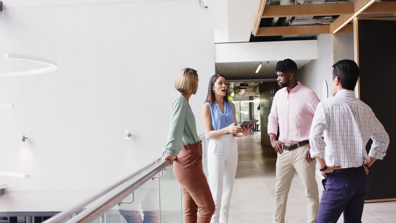 Group of business professionals discussing work, holding tablet in office hallway