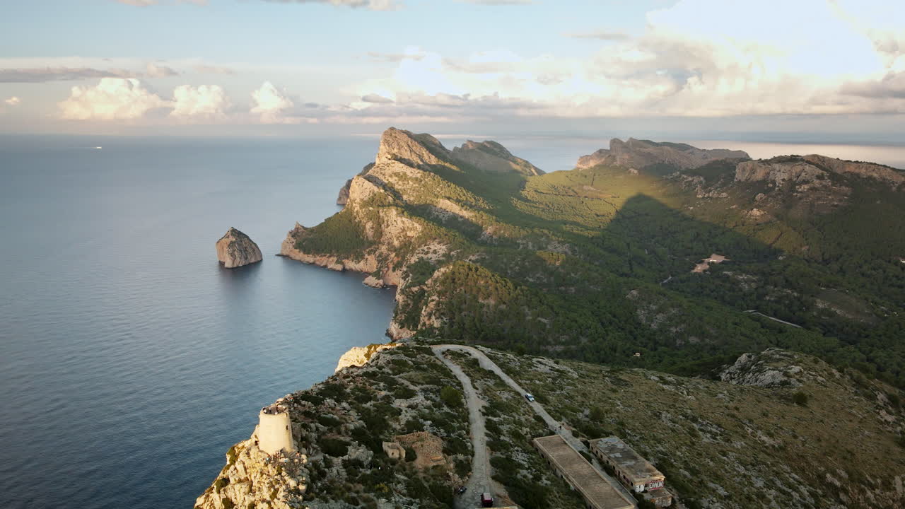 Un drone si muove in avanti verso la spettacolare penisola rocciosa e i pendii boscosi di Cap Formentor, planando sopra il calmo Mar Mediterraneo sotto la calda luce del tardo pomeriggio