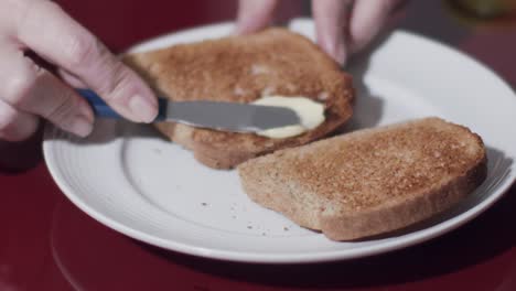 Hände-Eines-Kaukasischen-Modells,-Während-Butter-Auf-Einen-Toast-Geschmiert-Wird---Zeitlupe,-Nahaufnahme