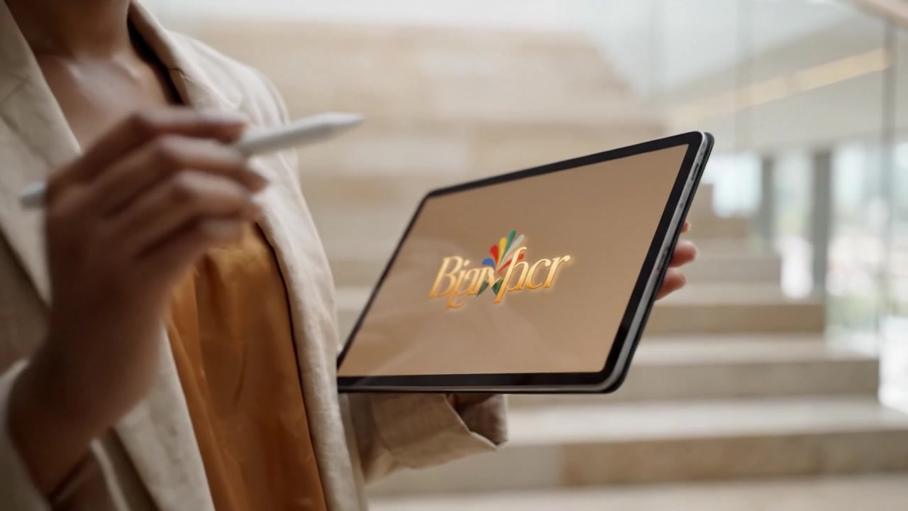 A focused woman in a beige blazer holding a tablet and stylus, engaged in digital work or note-taking while standing near modern architecture and stairs.