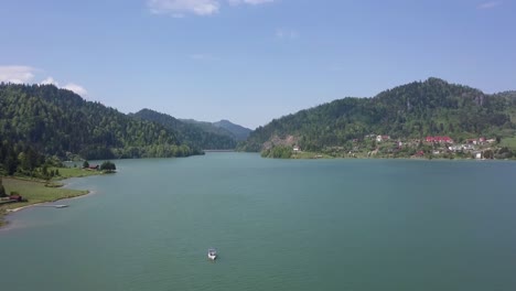 aerial panning shot of lake front with small boat in the foreground and valley in the background