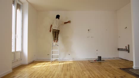 Hombre-En-La-Escalera-Pintando-La-Pared-Interior-De-La-Casa-Con-Pintura-De-Cal