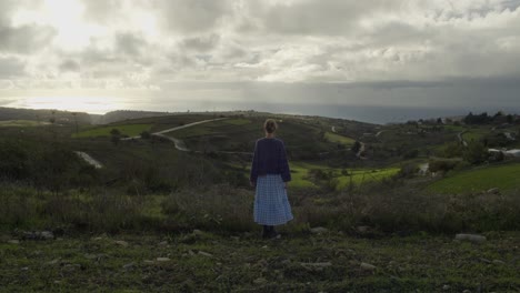 Una-Mujer-Joven-Mirando-El-Horizonte-Y-El-Mar-Mediterráneo-En-Un-Campo-Nublado-De-Chipre,-Cámara-Lenta