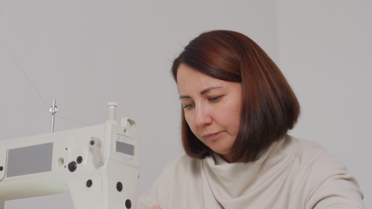 Needle woman carefully passing yard thread on sewing machine, focusing on skillful motion, precision, calm posture, and bright environment, highlighting craftsmanship in minimal workspace