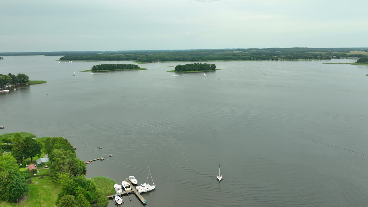 Aerial view of a rural lakeside area with small boats docked at the shoreline, houses nestled in green surroundings, and a wide lake with distant islands