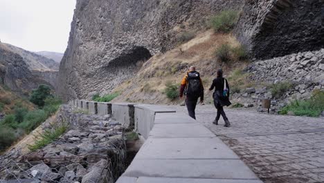 un hombre y una mujer pasan junto a columnas de basalto en el desfiladero de garni, armenia.