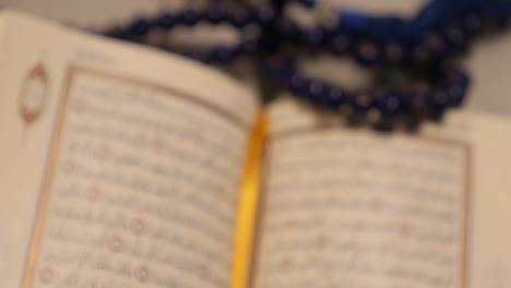 an open quran lying on a table with a prayer beads lying on it, the shot is approaching the quran