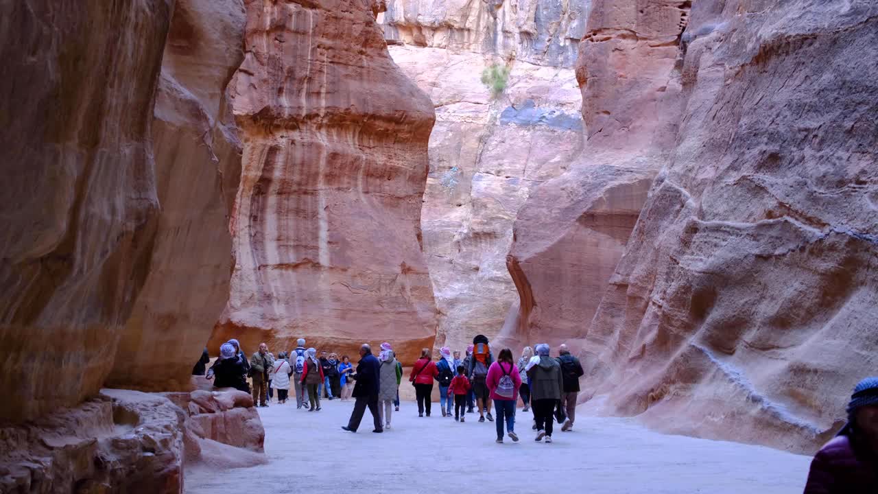 Groups of tourist visiting Petra and walking through narrow winding Siq Trail paths in Jordan