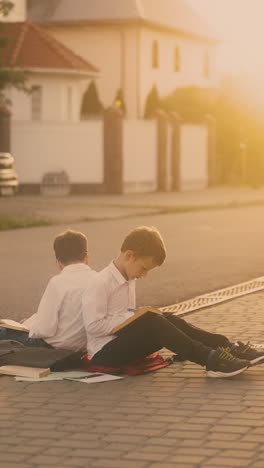 boys pupils sit on grey pavement read books and repel mosquitoes during preparation for exam against bright sunlight