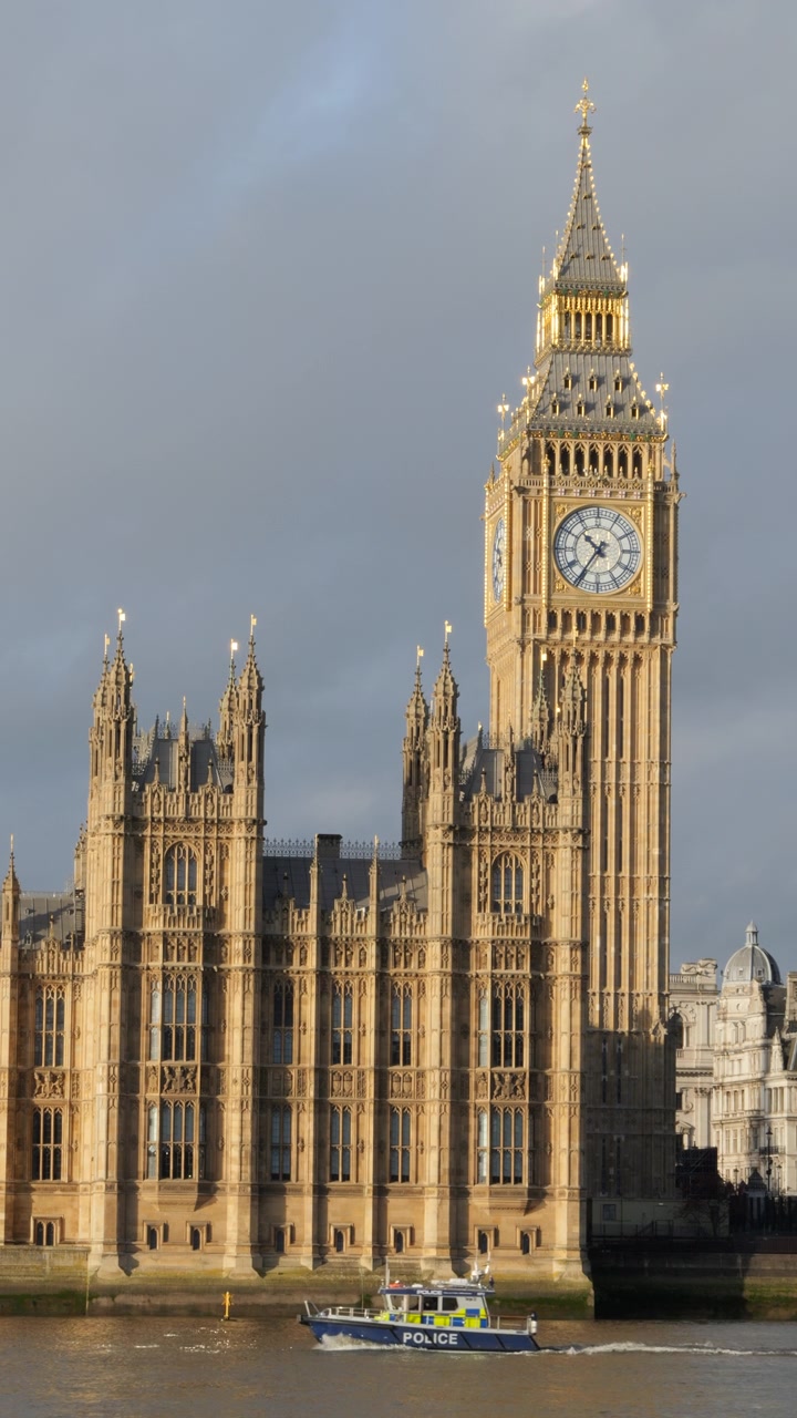 Politibåd sejler på Themsen, London, med Big Ben og Palace of Westminster i baggrunden. Lodret optagelse