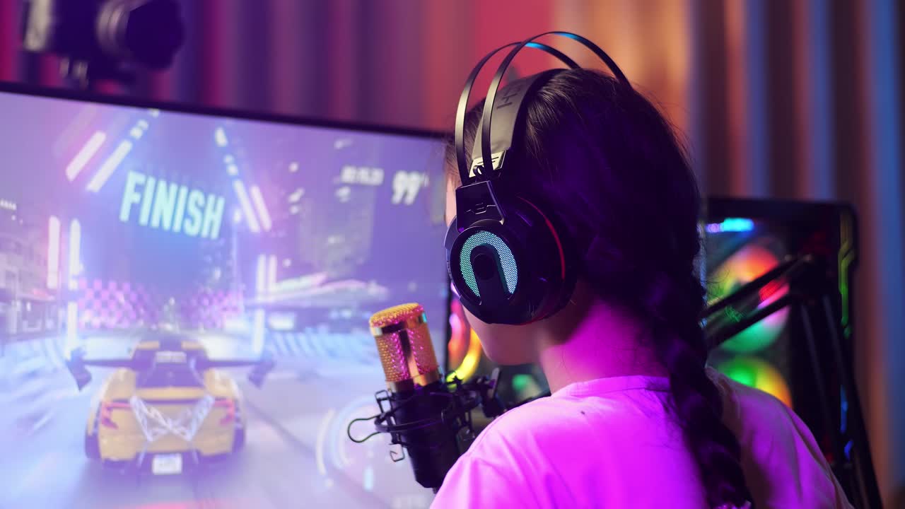 Vista ravvicinata da dietro di una streamer asiatica delusa che perde una partita di corse automobilistiche sul computer personale. Videogioco in live streaming, scrivania illuminata da striscia LED RGB.