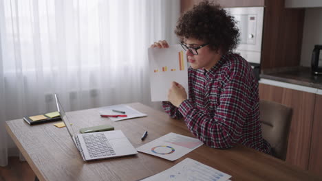 hombre de negocios de cabello rizado con gafas sentado en la oficina desde el escritorio de casa mirando a la cámara y apuntando a una tableta con información financiera mostrada en forma gráfica gráfico de columna