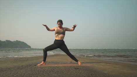 warrior 2 yoga pose being completed in slow mo by teacher on coastline