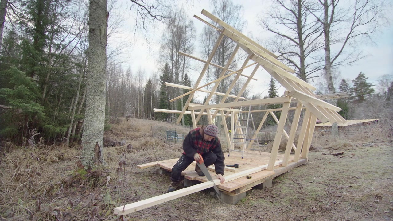 Yleismies sahaa puuta rakentaessaan omavaraista pientaloa metsässä.