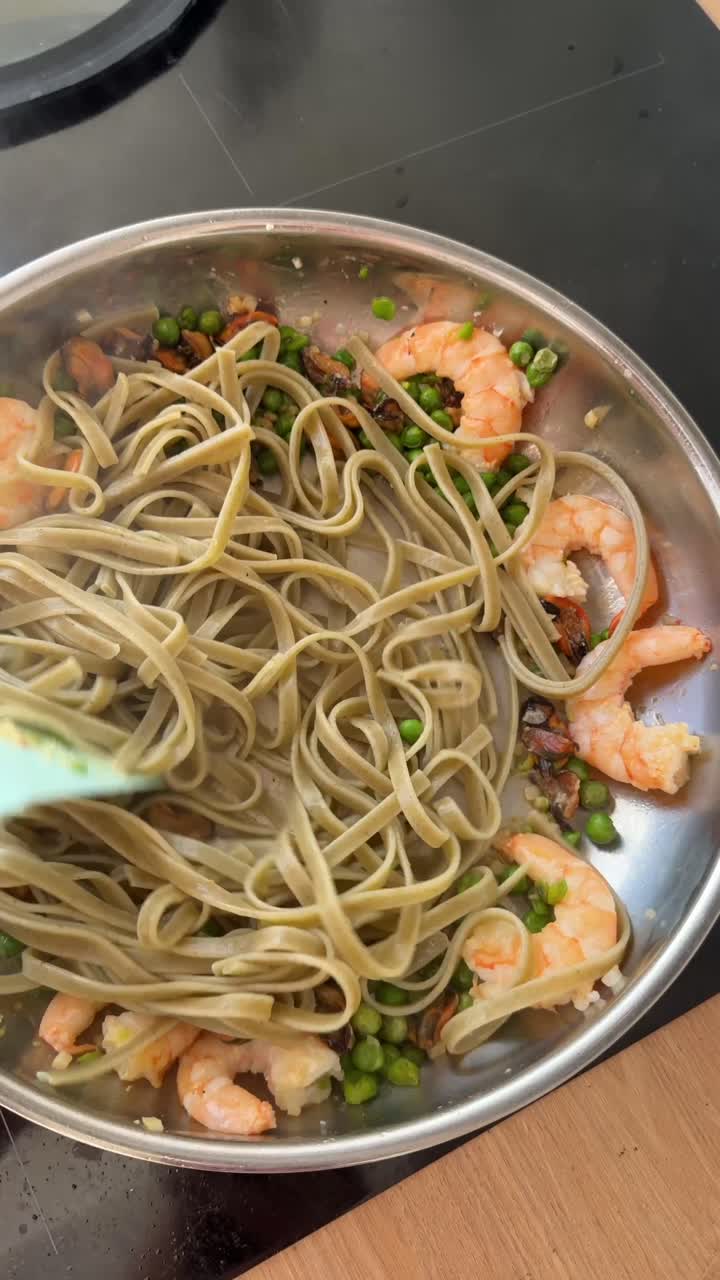 Pasta con gamberi e piselli e frutti di mare mescolata in padella