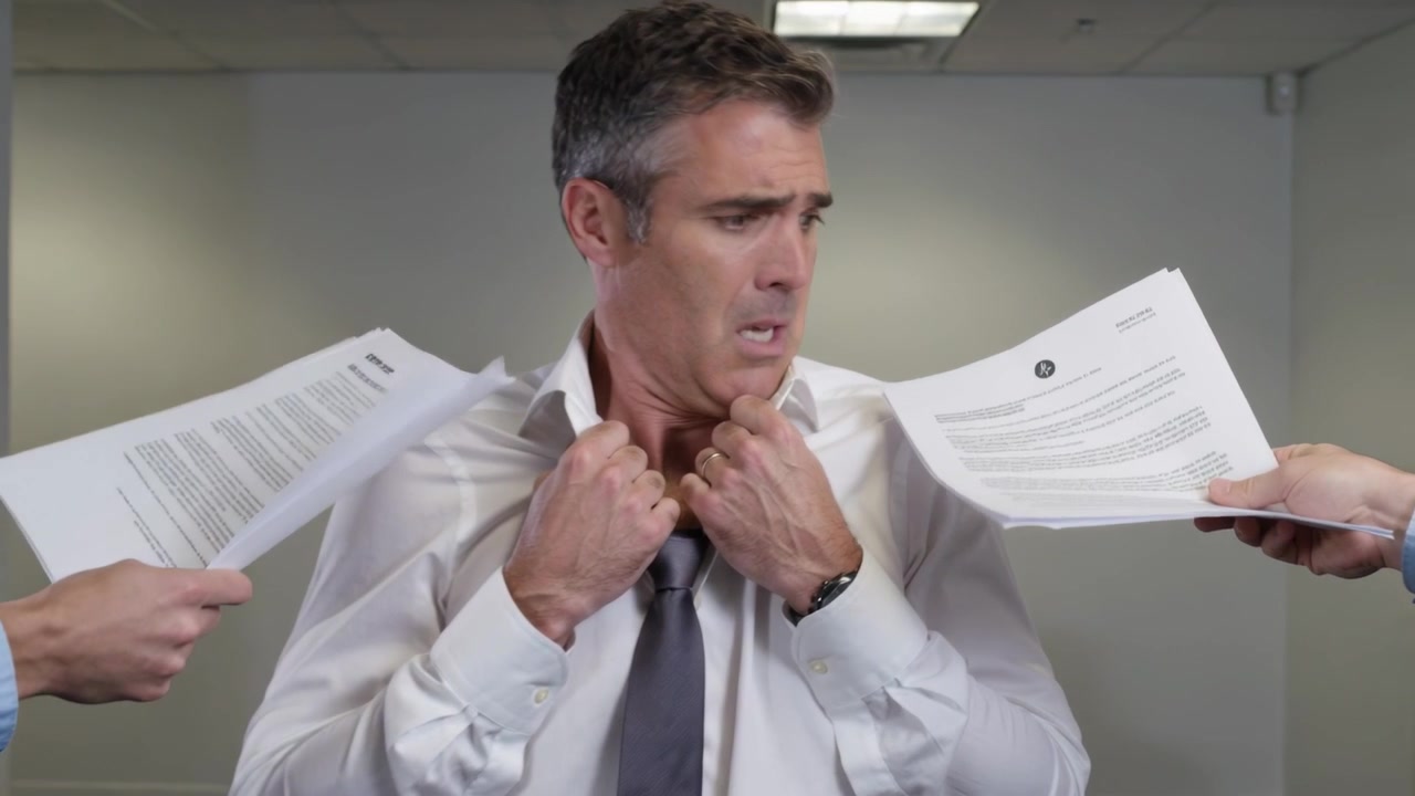 Mani che ricevono documenti offerti, uomo seduto che stringe la camicia bianca e la cravatta grigia alla scrivania, con un'espressione tesa.