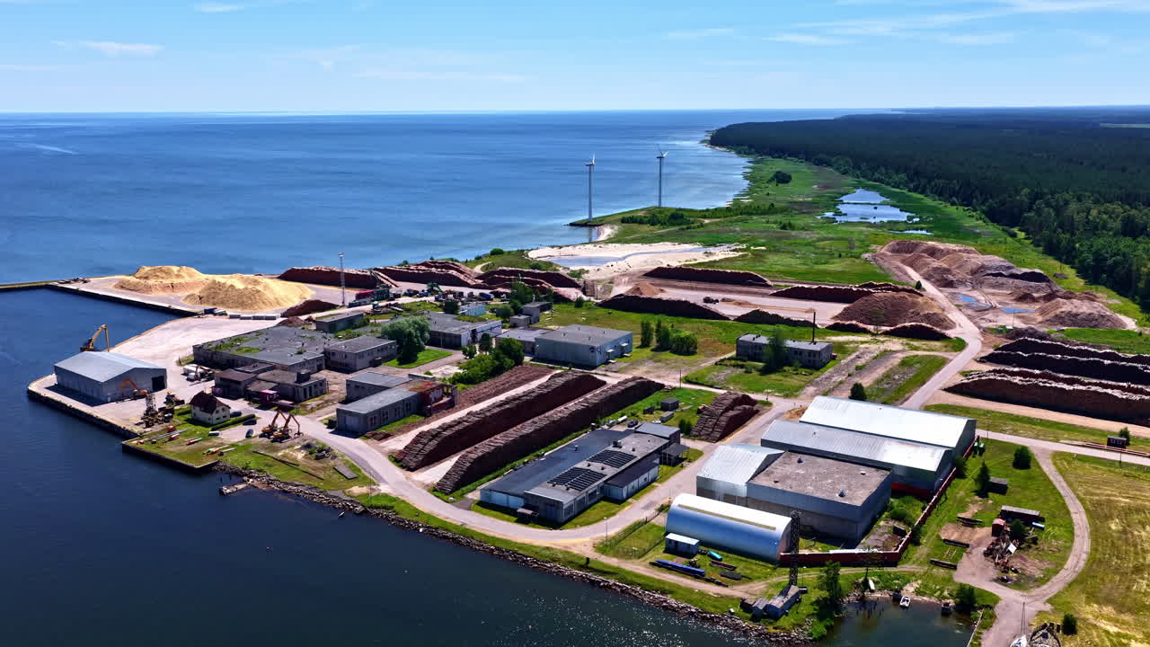 Aerial view of timber processing facility with wood stacks at coastline in Latvia