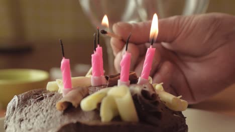 hand lighting candles on chocolate cake with match close up shot