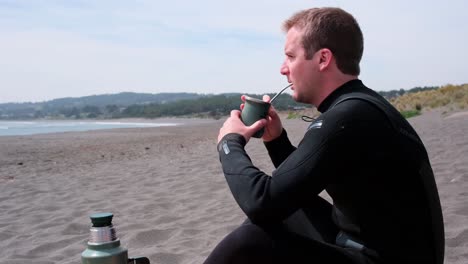 Mann-Trinkt-Argentinisches-Mate-Getränk-Am-Strand-Nach-Einer-Surf-Session-In-Chile-Pichilemu-Punta-De-Lobos-An-Einem-Sonnigen-Tag-Und-Trägt-Einen-Neoprenanzug