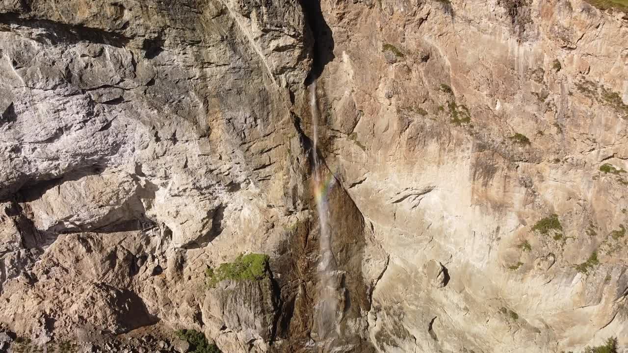 cascada de alta montaña desde la pared rocosa con colores del arco iris, toma aérea
