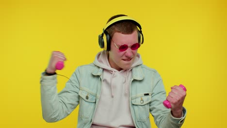 sporty teen student man listening music via headphones, working out, pumping up lifting dumbbells