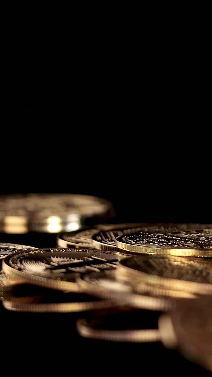 Multiple gold cryptocurrency coins fall and settle, captured in slow motion with dramatic lighting