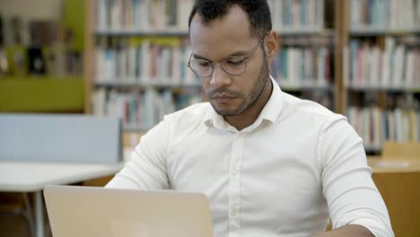 focused young man working with laptop in library