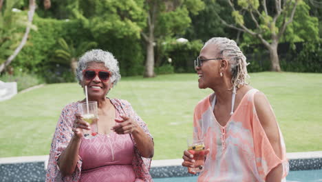 Felices-Amigas-Afroamericanas-Mayores-Con-Gafas-De-Sol-Y-Bebidas-Sentadas-Junto-A-La-Piscina,-Cámara-Lenta