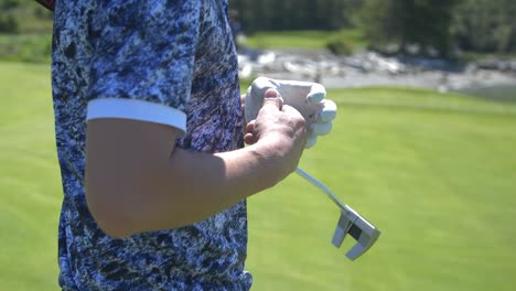 Golfer-confidently-removing-glove-preparing-for-putting-shot-on-green-on-sunny-day