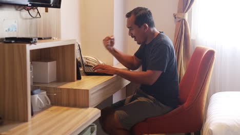 happy excited asian man working using laptop in hotel room