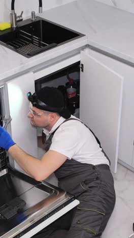 a plumber works lying on the floor in the kitchen he installs a sink the work of a plumber