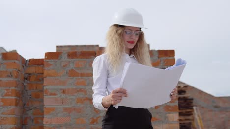 a female architect in business attire stands on the top floor in the open air at a construction site. the architect inspects the object according to the architectural plan