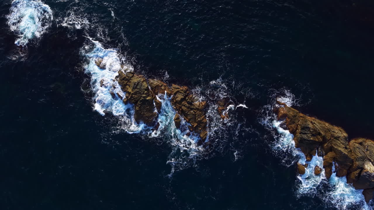 Waves crash against rugged rocks under a vast sky, capturing nature's beauty in a breathtaking coastal scene