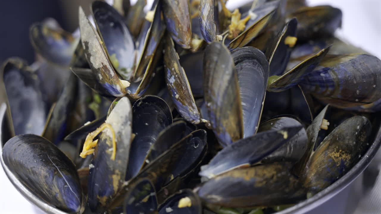 Close up of multiple steamy mussels in a pot with green onions on top