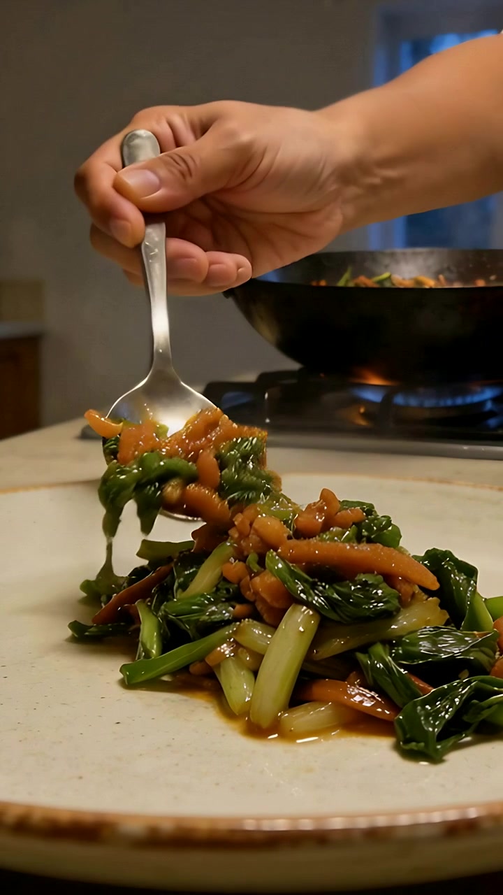 Vertical video: Scooping cook lifting spoon from wok at stove, plating vegetables on plate to serve