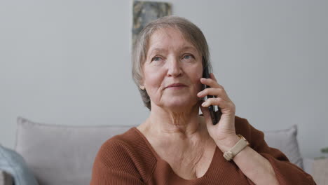 seniorin, die per smartphone anruft und zu hause sitzt