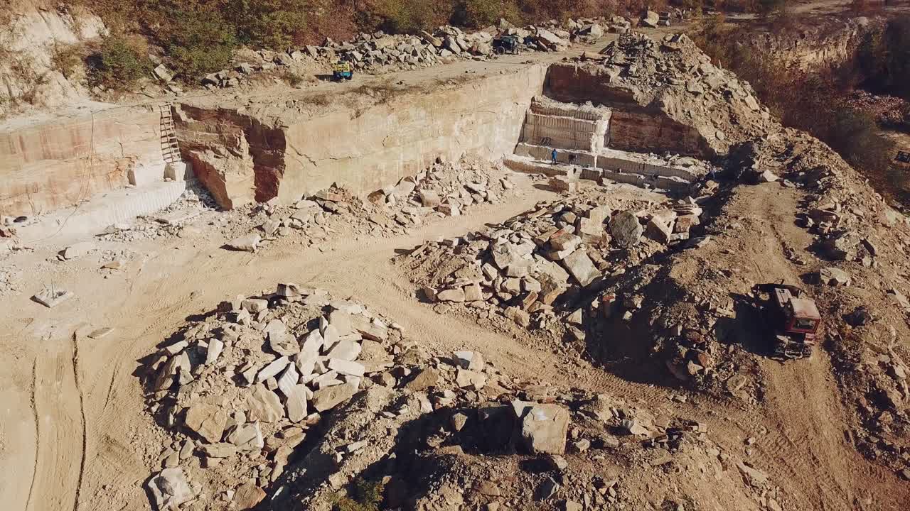 workers with professional equipment are working in the sandy quarry on the background of huge stones and a hill with trees. Camera motion up