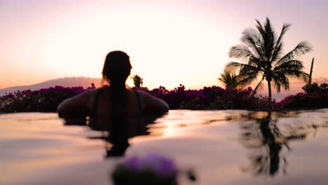 camera pans across infinity pool young tattooed island girl watches sunset behind island