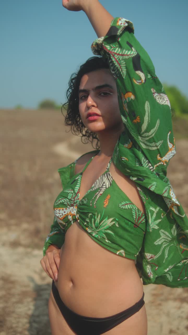 Woman posing outdoors in green printed shirt and black bikini bottom, sunny vibe