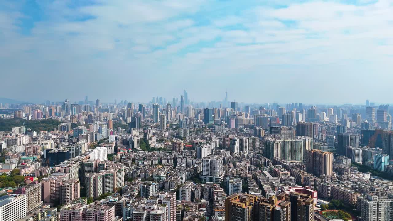 Wide drone shot of Guangzhou’s cityscape during daytime, featuring a vast skyline with modern skyscrapers, dense urban housing, and green spaces. China.