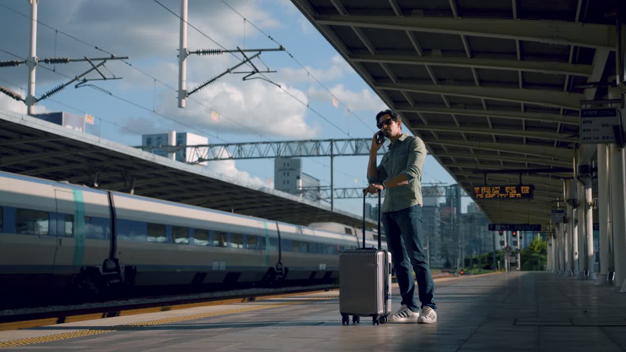 Casual stylish man talking on phone standing at Seoul train station, South Korea, solo traveler in urban transport hub, low angle pullback