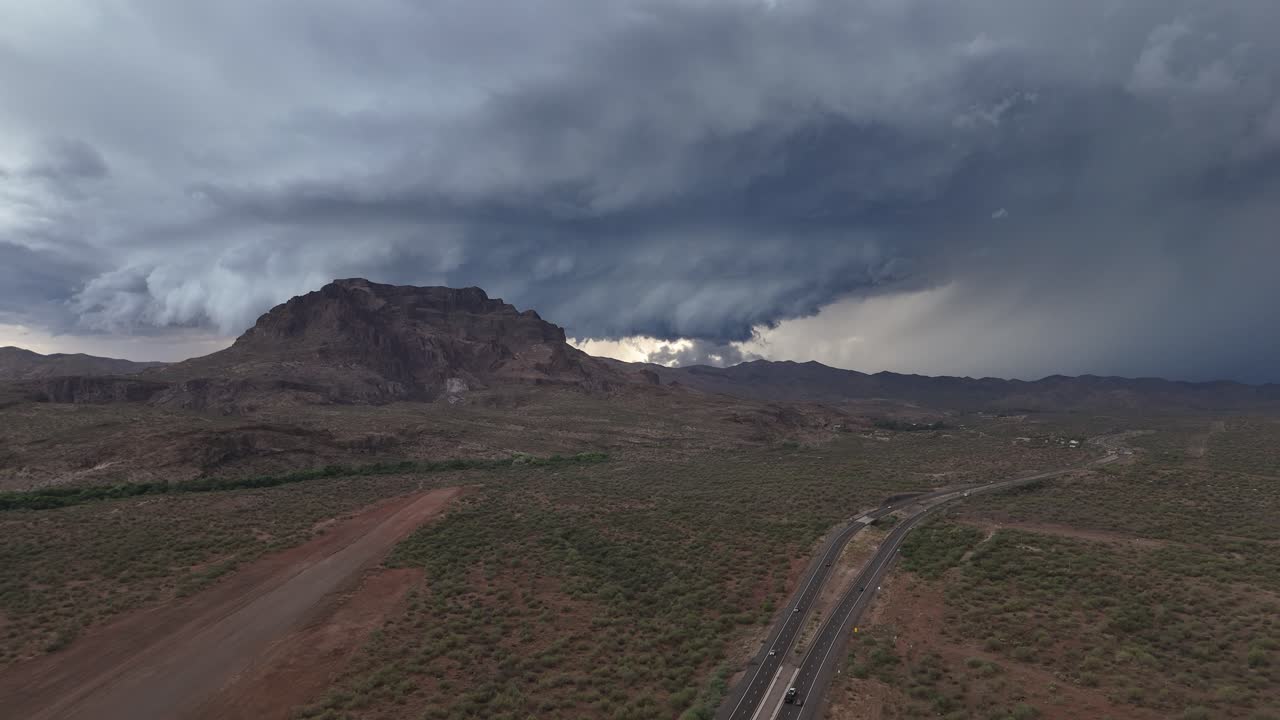 Aerial View of Desert with mountain and Storm Clouds in background, Cloudy skies, Highway off to side with few cars, lightning, Picketpost Mountain in Superior Arizona