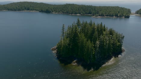 Imágenes-De-Drones-Rodeando-Una-Pequeña-Isla-En-Una-Bahía-Azul-Con-El-Sol-Reflejándose-En-El-Agua-En-El-Océano-Pacífico-Cerca-De-La-Isla-De-Vancouver,-Columbia-Británica,-Canadá