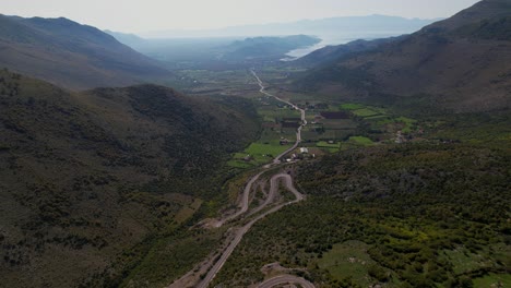 Beautiful-valley-with-the-road-between-green-fields-surrounded-by-high-mountains-and-the-lake-in-the-background,-Albania