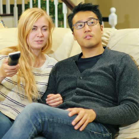 multi-ethnic young couple sitting on the couch watching tv together