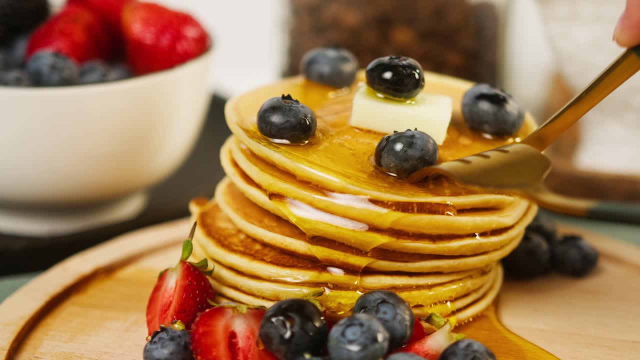 Tagliare una pila di pancake con frutti di bosco e sciroppo